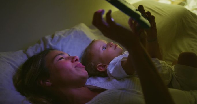 Authentic shot of happy neo mother and her newborn baby are using technology tablet for family entertainment in a bed before asleep. Concept of technology, new generation,family, connection,parenthood