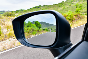 Close up of a rear view mirror with an empty road with mountains at the back