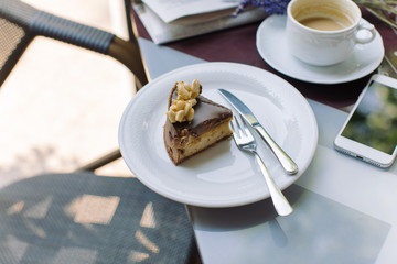 Piece of cake, cup of coffee and mobile phone on table in the cafe. Side view, copy space.