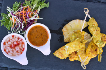 This unique photo shows the starter Chicken satay very stylishly presented on a black plate with 2 sauces and a salad. The chicken skewers are grilled