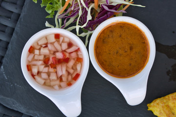This unique photo shows the two sauces that are served with the famous thai starter chicken satay in white containers on a black plate