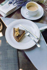 Cheesecake sliced and plated, cup of cappuccino, smart phone on table. Coffee break on summer terrace.