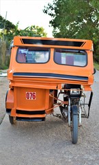 An empty orange tricycle is parked at the side of a concrete road in Coron, Palawan