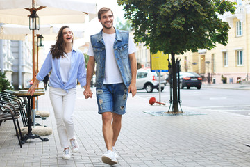 Image of lovely happy couple in summer clothes smiling and holding hands together while walking through city street.