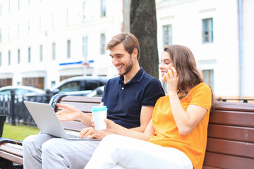 Attrative young couple using laptop computer while sitting on a bench outdoors.