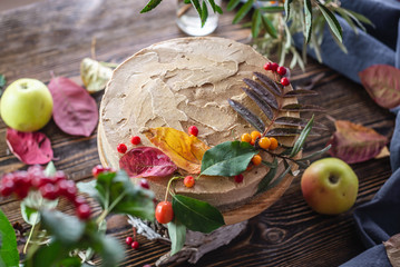 Brown mousse cake decorated with autumn leaves and berries. Wooden background. Concept of autumn...