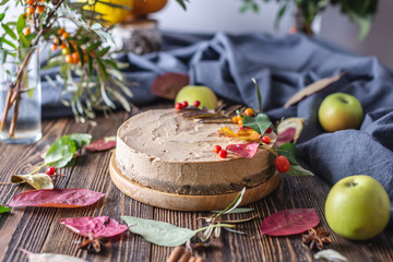 Brown mousse cake decorated with autumn leaves and berries. Wooden background. Concept of autumn mood and atmosphere