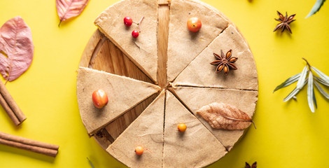 Brown mousse cake minimally decorated with autumn symbols on a yellow background. Concept of seasons and autumn mood