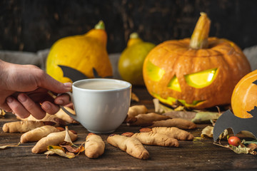 Cup of coffee with cookies fingers of a witch and a pumpkin on the table. Concept of Halloween and festive atmosphere