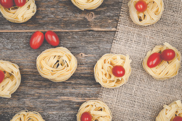 Nests of tagliatelle noodles with egg-shaped mini roma tomatoes on a rustic wooden table wit burlap
