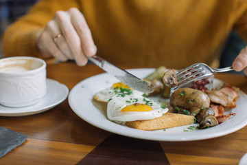 Man eating traditional English breakfast with fried eggs, sausages, beans, mushrooms, bacon at cafe in the morning.