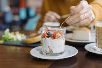 Man trying homemade granola, yogurt and fresh berries. Delicious breakfast at cafe on sunny day.