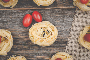Nests of tagliatelle noodles with egg-shaped mini roma tomatoes on a rustic wooden table wit burlap
