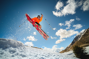 A young stylish man in sunglasses and a cap performs a trick in jumping with a kicker of snow...