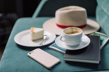 Lifestyle concept. Cup of coffee, smartphone, a piece of cheesecake, stylish female hat and notebook.