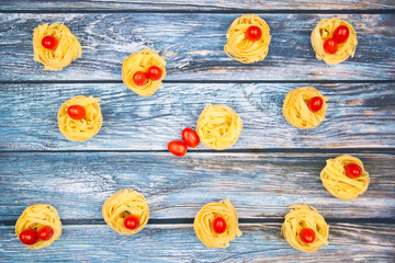 Nests of tagliatelle noodles with egg-shaped mini roma tomatoes  on a weathered bluish table.
