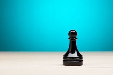 One black chess piece pawn on wooden table against blue background