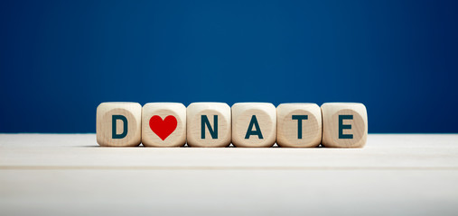 The word donate on wooden blocks with heart icon against blue background. Charity and donation.