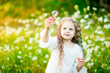 little beautiful girl playing on the lawn in summer with soap bubbles