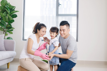 Fototapeta premium Mom, dad and their little daughter cleaning living room together.