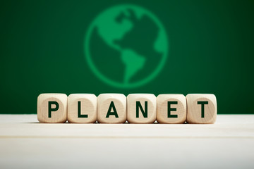 The word planet on wooden cubes against green background with earth icon. Planet earth ecology concept.