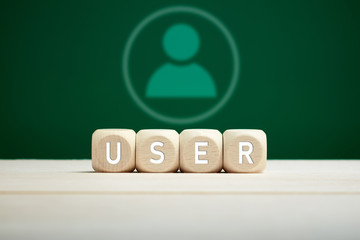 The word user on wooden blocks against a user icon on green background. Technology, communication or internet user concept.