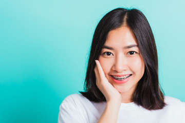 Portrait of Asian teen beautiful young woman smile have dental braces on teeth laughing she touching her face by hand, studio shot isolated on a blue background, Medicine and dentistry concept