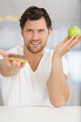 young man holding apple and unhealthy donut