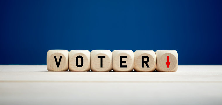 The word voter with downward arrow on wooden cubes. Elections and decreasing voter turnout concept.