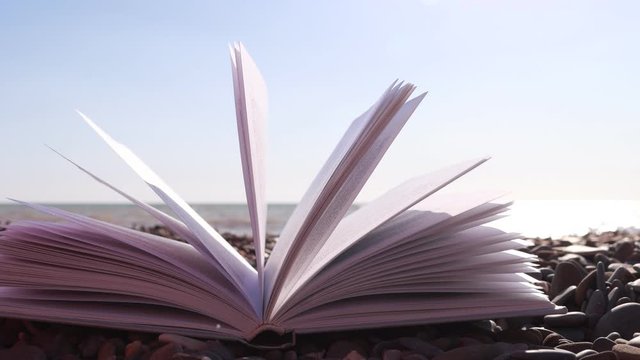 Fluttering pages of an open book with the sea waves on the background