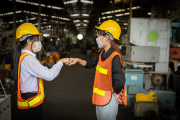 Two factory trainees with face mask giving fist bump to appreciate each other. Factory in new normal to prevent Coronavirus or COVID-19 infection