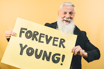 Happy youthful senior feeling forever young - Hipster mature man giving message with yellow banner...