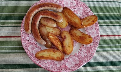Sausages and halves of potatoes fried over the fire are laid out on a plate in the fresh air