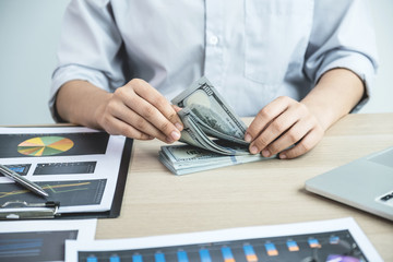 Businesswoman hands count dollar note and analysis the chart with laptop at the office for setting challenging business goals And planning to achieve the new target