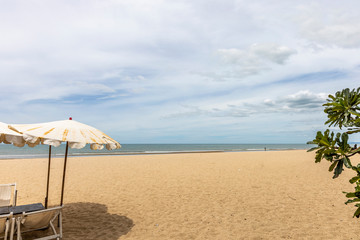 Beach umbrella at foreground. Scenic view of empty tropical sandy and peaceful beach under cloudy blue sky with light turquoise waves.