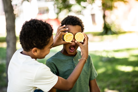 Two boys are playing with a lemon, making a lemon eye face on a sunny day