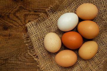 Fresh colorful chicken eggs on a natural wooden background and mat. Food background, top view. Place for text.