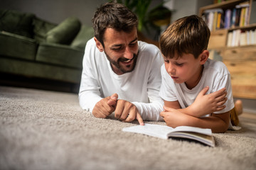 Father and son read a book together, father smiles while son reads, education at home