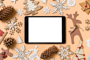 Top view of digital tablet surrounded with New Year toys and decorations on orange background. Christmas time concept