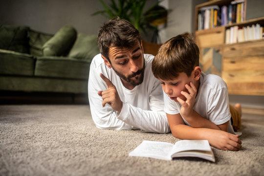 Father and son read a book together, father explains to son, education at home - Powered by Adobe