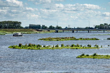 Naklejka premium Kampen, The Netherlands, July 26, 2020: view across the new Reevediep river channel, with small islands, a bridge and a small yacht
