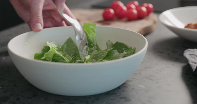Slow motion man hands making caesar salad in white bowl , mix romaine with dressing