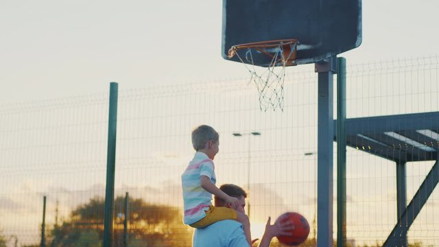 Dad and son playing basketball at sunset