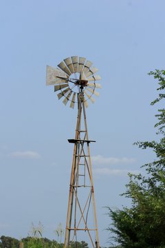 old windmill in the field with tree's and blue sky with tree's in Kansas.