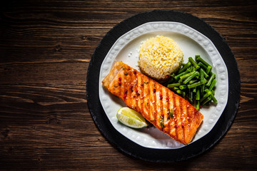 Fried salmon steak with rice and vegetables on wooden table
