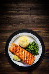 Fried salmon steak with rice and vegetables on wooden table
