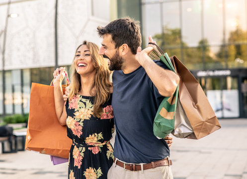 The couple is carrying bags with things they bought in the shopping mall, with a smile on their face