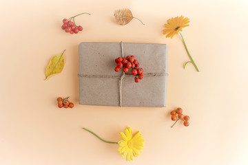 Autumn flat lay composition. Pretty gift box wrapped with craft paper and decorated with flower on orange background among dry foliage. Thanksgiving day concept. Copy space. Selective focus