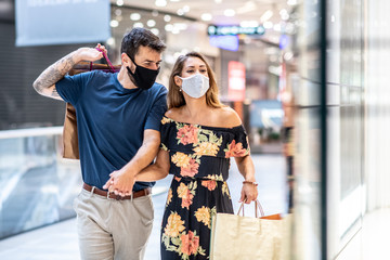 A young couple is carrying shopping bags with masks on their faces and walks, shopping during a pandemic