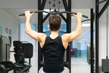 Fototapeta premium Man using a lat machine in a gym to train his shoulders and back, bodybuilding and natural fitness concept